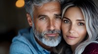 Mature couple with silver hair embracing, close-up portrait showing genuine connection. Man with gray beard and woman in burgundy top display authentic emotions.