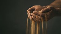 Elderly hands resting on wooden walking cane handle showing aging, wisdom and senior care needs with warm dramatic lighting on dark background.