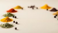 Colorful spices and herbs arranged in small piles on white background creating culinary ingredient display for cooking and seasoning recipes.