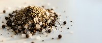 Ground black pepper pile with whole peppercorns scattered on white surface for culinary seasoning and cooking ingredient photography.