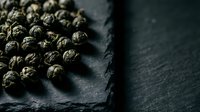 Dried allspice berries arranged on dark slate surface with dramatic lighting and shadows, suitable for culinary, food styling, and spice ingredient photography.