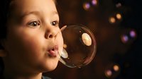 Young child blowing soap bubbles with colorful bokeh lights in background creating magical childhood moment for family and play concepts.