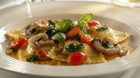 Fresh ravioli pasta with mushrooms, cherry tomatoes and basil in light butter sauce on white plate, close up view of traditional Italian cuisine.
