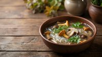 Homemade mushroom soup with fresh herbs served in rustic wooden bowl on kitchen table. Comfort food for cold weather dining and healthy eating lifestyle.