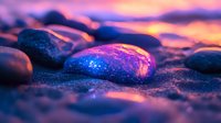 Smooth pebbles on beach sand at sunset with vibrant purple and orange sky reflections creating magical atmosphere and bokeh effect on wet stones.