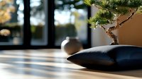 Minimalist zen composition with bonsai tree and black meditation cushion on wooden table, soft natural lighting creates peaceful shadows and atmosphere.