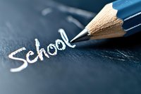 White chalk written word school with blue wooden pencil on dark chalkboard surface, macro photography with selective focus and shallow depth of field.