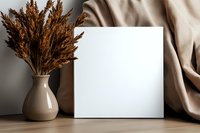 Blank white square canvas mockup with dried pampas grass in beige ceramic vase and draped fabric on wooden surface, modern minimal home decor styling.