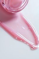 Pink cosmetic serum texture with glass jar on white background, showing luxurious skincare product with glossy, pearlescent finish and subtle bubbles.