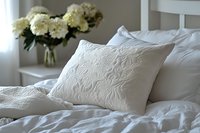 White embossed decorative pillow on bed with floral pattern quilted texture for bedroom interior design and home decor styling.