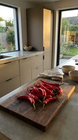 Modern kitchen interior with fresh red chili peppers on wooden cutting board, contemporary cabinetry and large windows overlooking garden for culinary design.