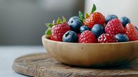Fresh mixed berries including strawberries, blueberries and raspberries in wooden bowl on rustic cutting board against light background, healthy food.