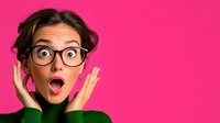 Young woman with shocked surprised expression wearing glasses against pink background, hands on cheeks with open mouth and wide eyes showing excitement.