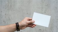 Caucasian male hand holding blank white business card against weathered concrete wall background for branding mockup.