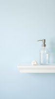 Minimalist bathroom shelf with clear glass soap dispenser, white towel, and seashell on light blue wall background for spa and wellness design projects.