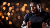 Athletic African American man in black t-shirt running or exercising against dark background with golden bokeh lights creating dramatic atmosphere for fitness and wellness concept.