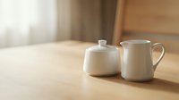 White ceramic teapot and creamer pitcher on wooden table with soft natural light, suitable for tea service, hospitality, and tableware design projects.