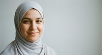 Young Muslim woman in white hijab smiling warmly at camera against neutral background for professional headshot and diversity content.