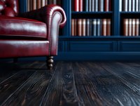 Burgundy leather armchair with brass studs against dark wood flooring and blue bookshelf background creates luxurious study or library atmosphere.