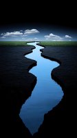Meandering river flows through dark landscape under cloudy sky, creating dramatic contrast between blue water and black shores with green grass horizon.