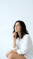 Young Hispanic woman in white shirt smiling and looking up thoughtfully against clean white background for lifestyle and wellness concepts.