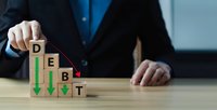 Businessman arranging wooden blocks spelling DEBT with downward arrows showing financial decline and economic crisis management strategies.