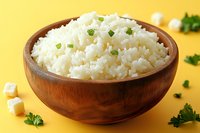 Steamed white rice garnished with chopped green onions in wooden bowl on bright yellow background, traditional Asian cuisine side dish.