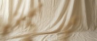 Soft beige linen fabric draped elegantly with natural wrinkles and folds creating organic texture for minimalist photography backdrop and product display.