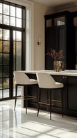 Modern luxury kitchen interior with black cabinets, white marble countertop, cream barstools and floor-to-ceiling windows. Natural light creates dramatic shadows on polished floors.