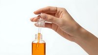 Hand holding glass dropper bottle with amber essential oil or serum against white background for skincare and wellness applications.