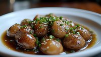 Glazed Asian meatballs garnished with fresh chopped green onions and sesame seeds in savory soy sauce, served on white ceramic plate, macro food photography.
