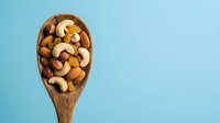 Mixed nuts and dried fruits in wooden spoon on blue background. Healthy snacking, organic food ingredients for cooking and baking recipes.