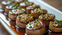 Grilled mushrooms glazed with Asian sauce and topped with sesame seeds and fresh green onions on white serving plate, close up view with selective focus.