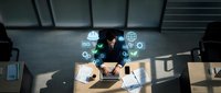 Businesswoman working at desk with laptop and digital icons representing global connectivity, technology, and business solutions.