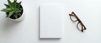 Minimalist white workspace with blank notebook, eyeglasses and green plant on clean desk surface for business planning and creative writing projects.