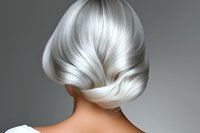 Elegant platinum silver hair styled in a smooth updo shown from behind on gray background, highlighting professional salon work and modern hair coloring technique.