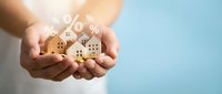 Hands holding miniature wooden houses with percentage symbol representing mortgage rates, real estate investment and property financing concepts.
