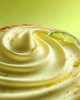 Creamy lime dessert with swirls of smooth custard, fresh citrus slice and crumbled cookie crust against vibrant green background.