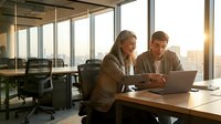 Professional businesswoman and businessman collaborating on laptop in modern office conference room with city skyline view during golden hour sunset.