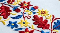Traditional folk embroidery with colorful floral motifs on white fabric. Handcrafted textile art featuring red, blue and yellow thread work for cultural decor.