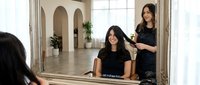 Asian woman getting professional hair styling service from female hairstylist in modern salon with mirror reflection and natural lighting.
