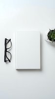 Minimalist white workspace with blank book, black eyeglasses and small potted plant on clean desk surface for business branding and design mockups.