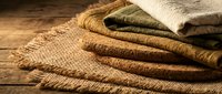 Stack of natural jute and burlap fabric textiles with frayed edges on rustic wooden surface for eco-friendly crafting and home decor projects.