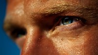 Close-up of intense blue eye with weathered skin texture against deep blue background, capturing determination and life experience.