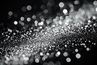 Abstract black and white bokeh background with glowing defocused light spots creating magical sparkle effect, suitable for festive designs and luxury backdrops.