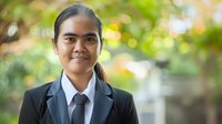 Young Asian businesswoman in formal suit and tie smiling confidently at camera with natural bokeh background, representing professional success and corporate leadership.