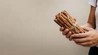Bundle of cinnamon sticks held in hands against neutral background. Spice ingredient for cooking, baking, and culinary use.