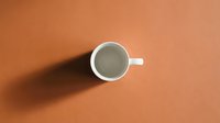 White ceramic coffee cup with shadow on warm orange background, minimalist flat lay composition for branding and marketing materials.