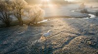 Frost-covered rural landscape with winding river and bare trees at sunrise, showcasing winter scenery for nature and seasonal design projects.