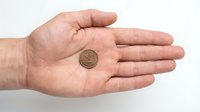Male hand holding small bronze coin on palm against white background, showing currency exchange or financial savings concept.